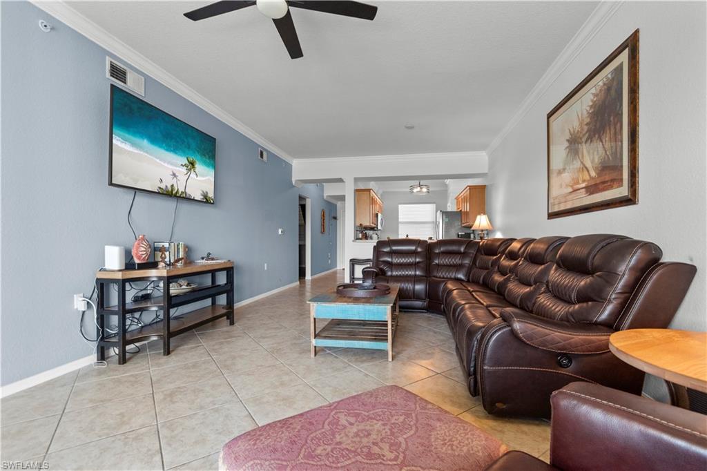 Spacious living area featuring tiled flooring, a ceiling fan, crown molding, and a wall-mounted television