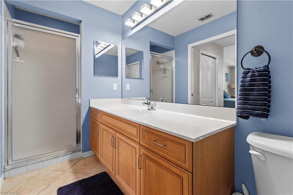 Primary bathroom featuring a shower with frosted glass enclosure, a wood-finish vanity with a white countertop, a large wall-mounted mirror, and tile flooring