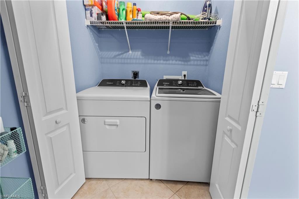 Dedicated laundry area featuring a washer and dryer, tiled flooring, light blue walls, and a white wire shelving unit
