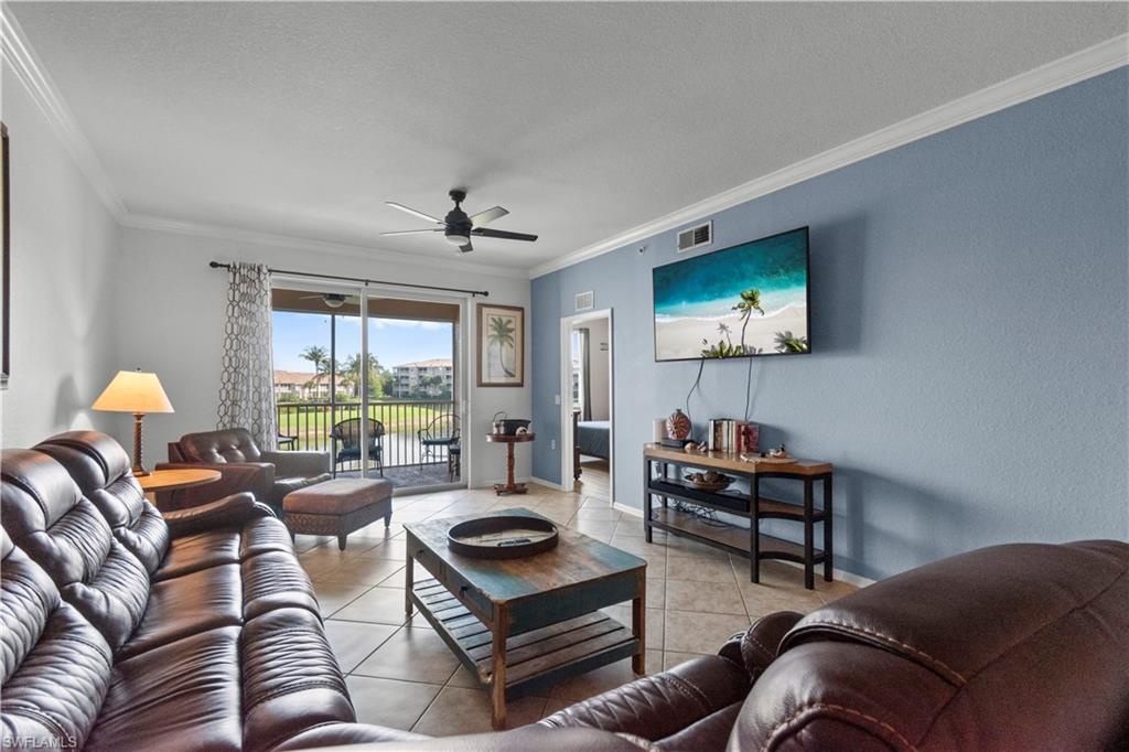 Spacious living area featuring neutral tile flooring, a ceiling fan, and crown molding