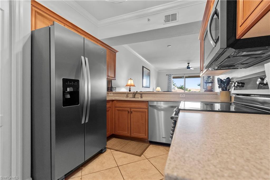 Kitchen featuring stainless steel appliances, wood cabinetry, stone countertops, and tile flooring