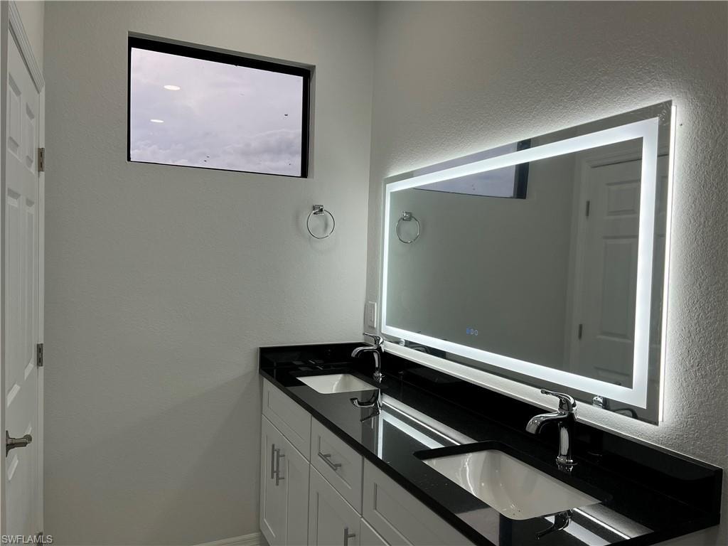 Dual vanity with white cabinetry, black countertop, dual undermount sinks, and chrome faucets