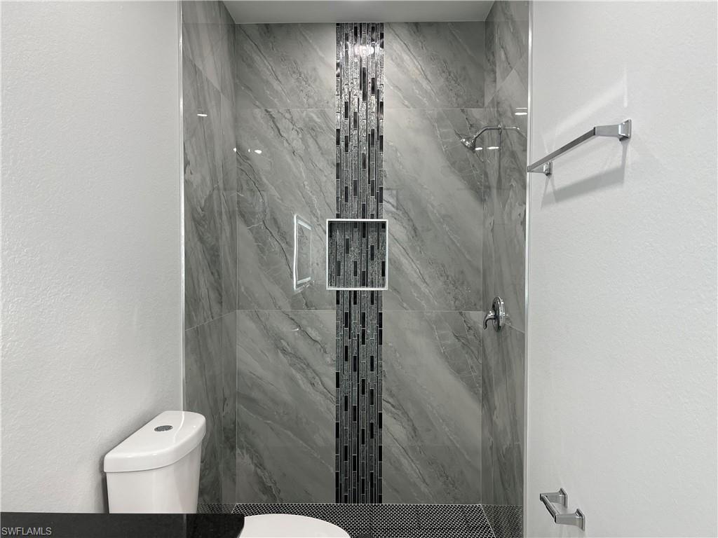 Walk-in shower featuring large format tile with a mosaic accent strip and built-in niche