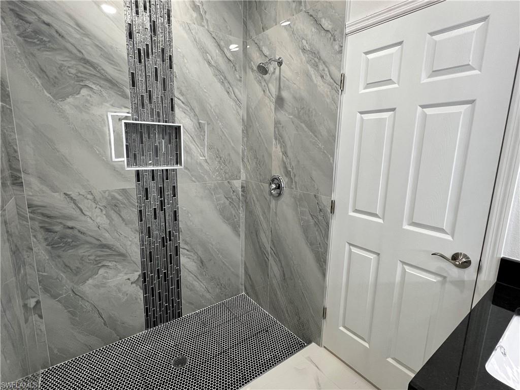 Walk-in shower featuring large format grey veined tile, a vertical accent of linear mosaic tiles, and a recessed niche
