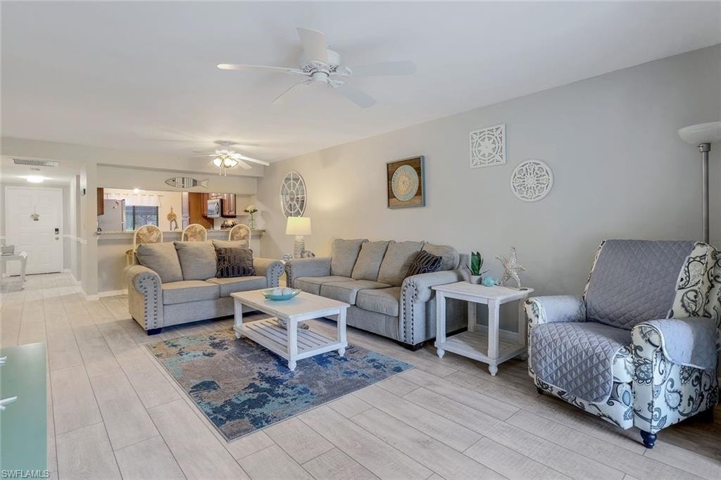 Bright open-concept living space featuring wood-finish flooring, a ceiling fan with integrated lighting, and a breakfast bar with recessed lighting
