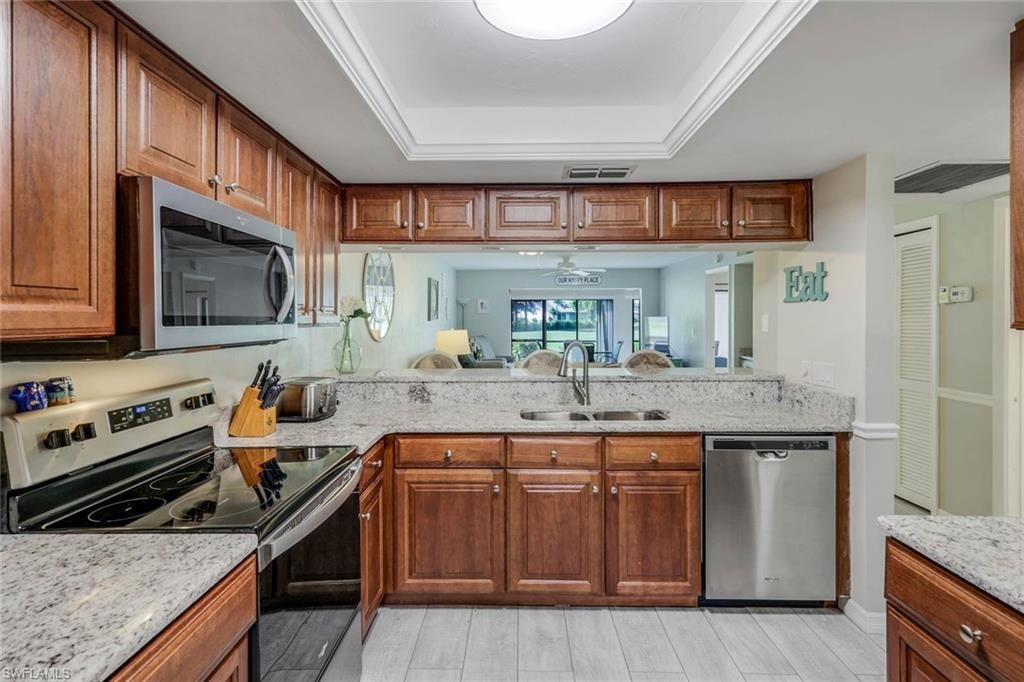 Kitchen featuring wood cabinetry, light-toned countertops, tile flooring, and stainless steel appliances including a built-in microwave, range, and dishwasher