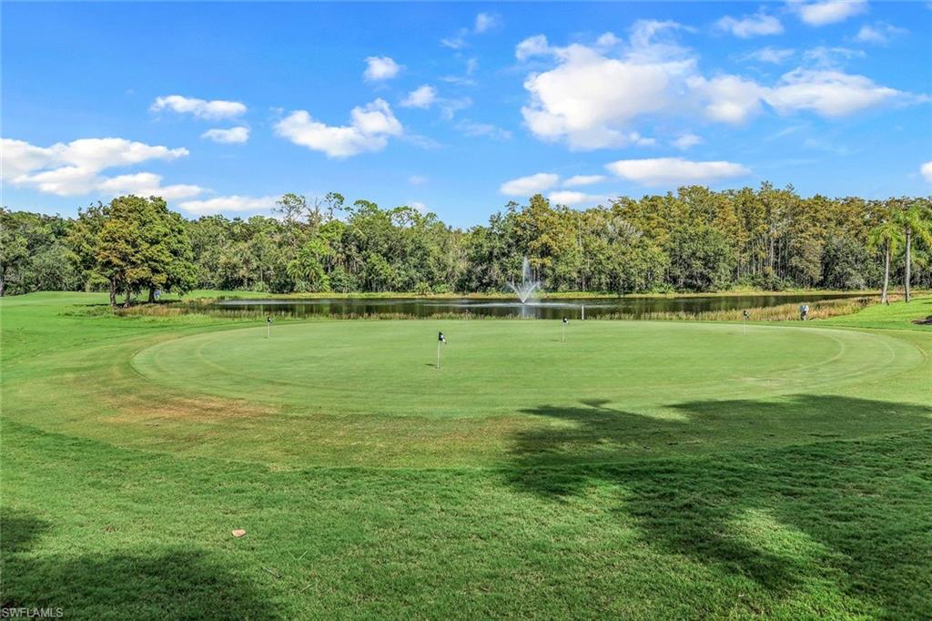 Expansive golf course green with multiple flagsticks, bordered by a tranquil pond featuring a water fountain