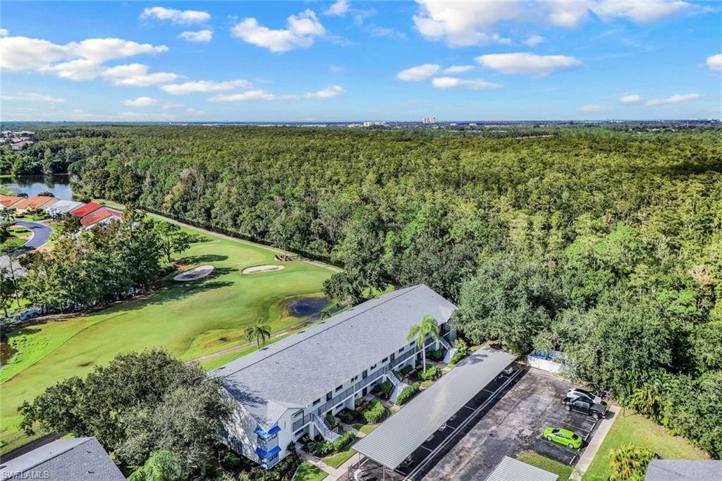 Aerial perspective showcasing a multi-unit residential building bordered by expansive woodlands and golf course greens