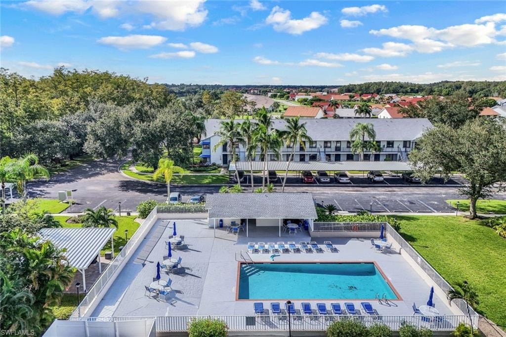 Outdoor swimming pool area featuring a perimeter fence, multiple lounge chairs, and umbrella-covered tables