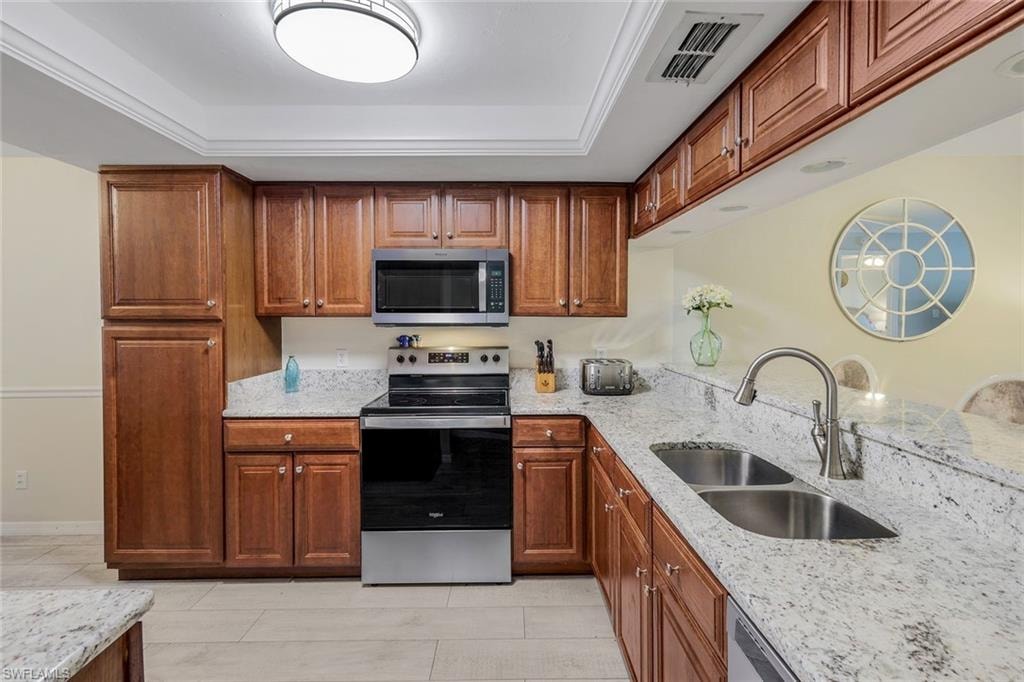 Kitchen featuring wood cabinetry, light-toned granite-style countertops, stainless steel appliances, and a double-basin sink with a gooseneck faucet