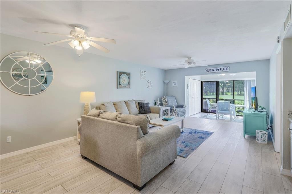 Expansive living area with wood-finish flooring, two ceiling fans, and a large window opening to outdoor space