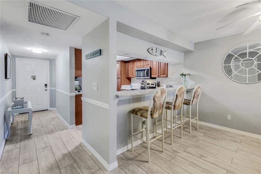 Open-concept living area featuring wood-finish flooring, a kitchen pass-through with a breakfast bar, and a ceiling fan