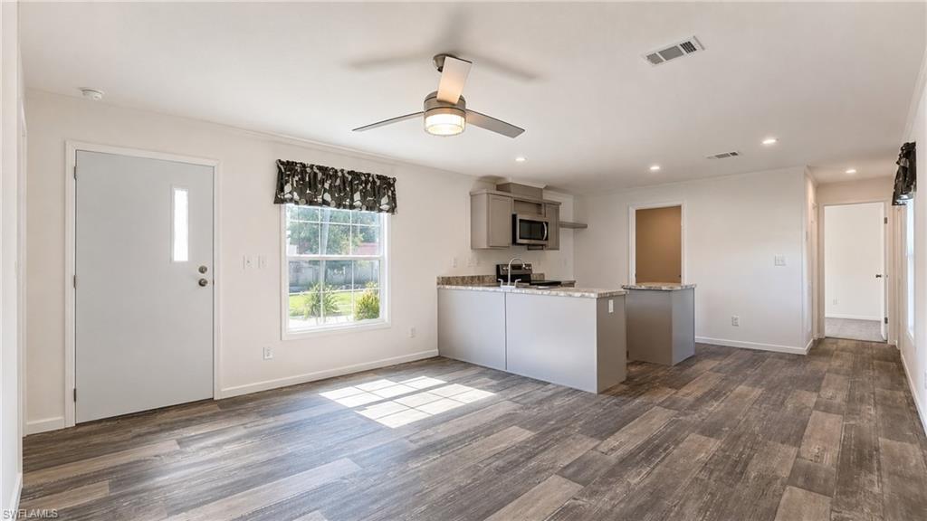 Open-concept living space featuring wood-finish flooring, a contemporary ceiling fan, recessed lighting, a kitchen island with seating, and a built-in microwave
