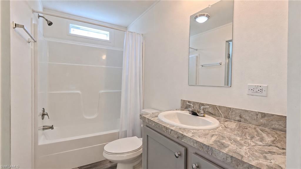 Full bathroom featuring a white tub/shower combination with an upper window, a toilet, and a vanity with a countertop and under-sink cabinetry