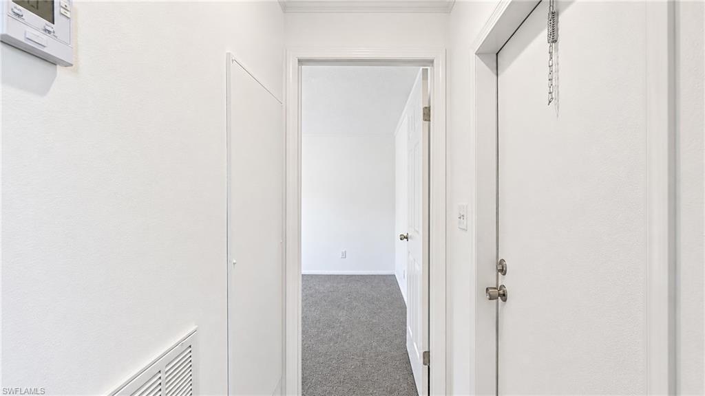 Interior hallway featuring white painted walls and trim, a white door with brushed nickel hardware, and a digital thermostat