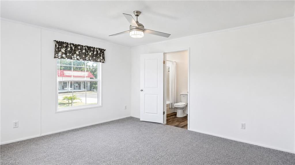 Spacious room featuring gray carpeting, white walls, a ceiling fan with integrated lighting, and a window with a valance