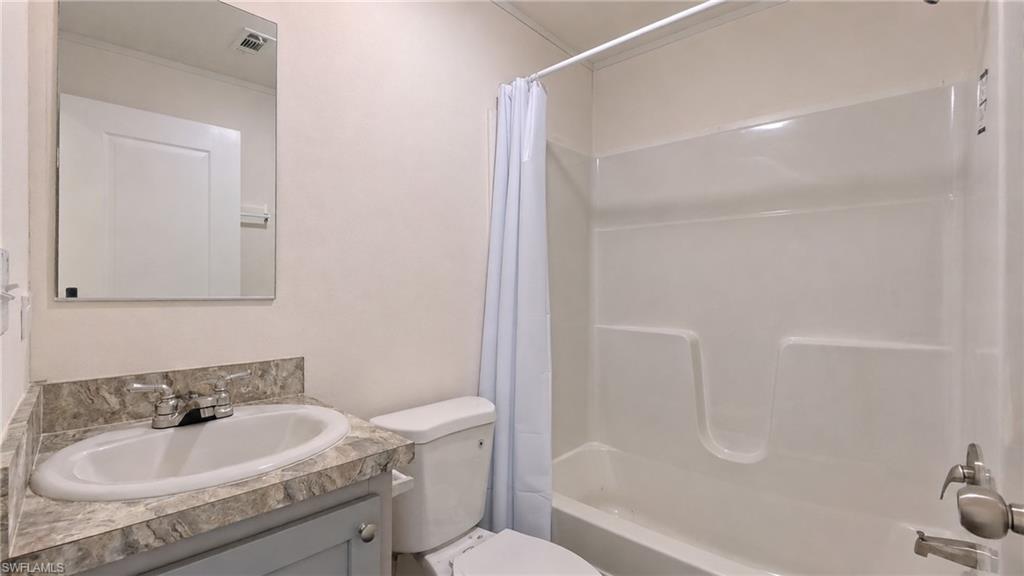 Full bathroom featuring a single vanity with a patterned countertop and white basin, a toilet, and a white tub/shower combination with a shower curtain rod