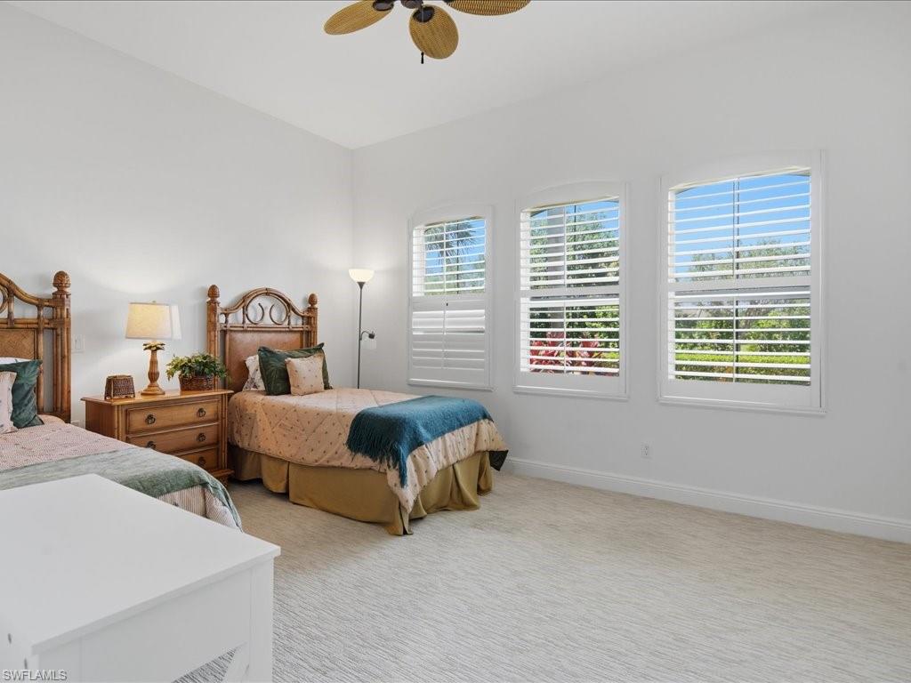 Spacious room featuring three arched windows with white plantation shutters, a vaulted ceiling, a ceiling fan, and light-toned patterned carpeting