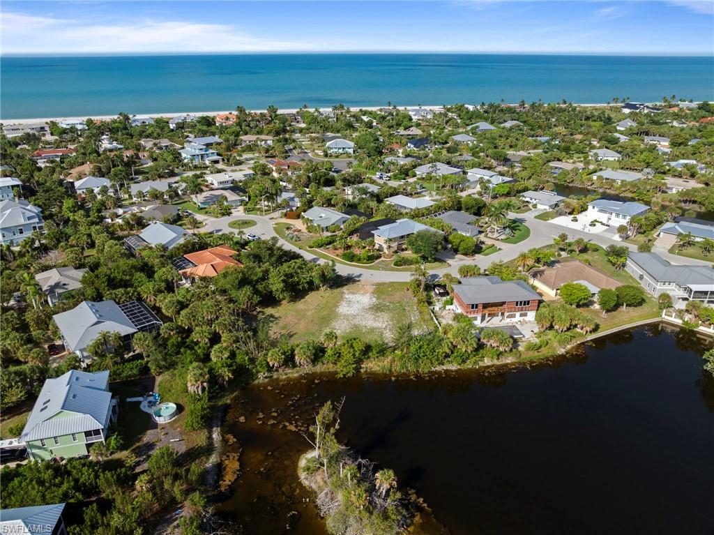 Expansive community setting featuring a coastal shoreline, residential properties, mature trees, a circular street layout, and a body of water