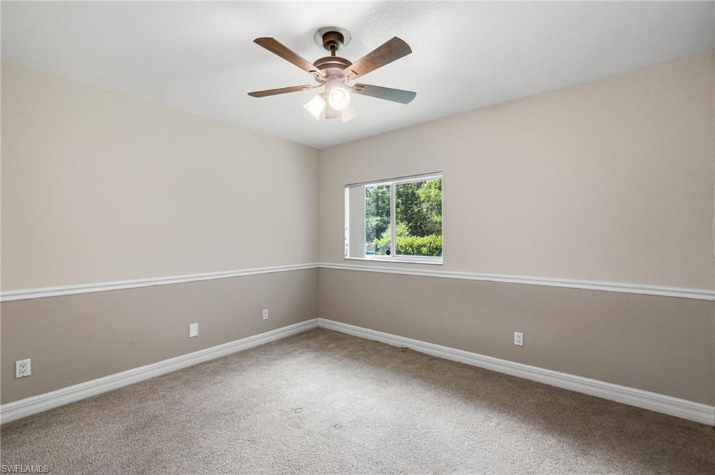 Carpeted interior space featuring a ceiling fan with light fixture, window, and two-tone wall treatment with decorative trim