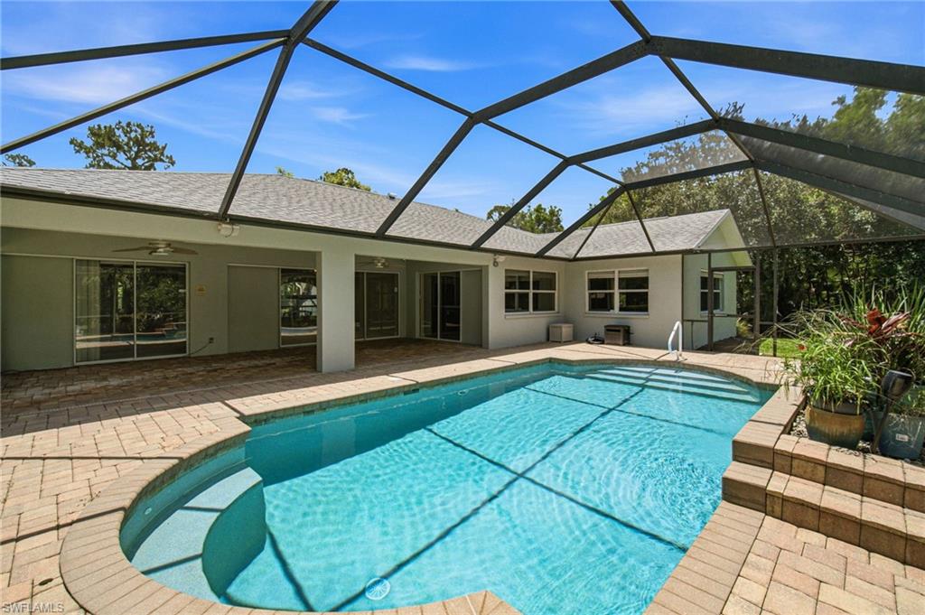 Enclosed pool area featuring an in-ground swimming pool, brick paver decking, and a screened enclosure