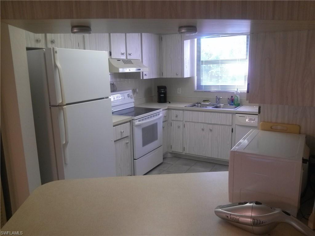 Kitchen featuring tasteful backsplash, white appliances, light tile flooring, sink, and white cabinetry