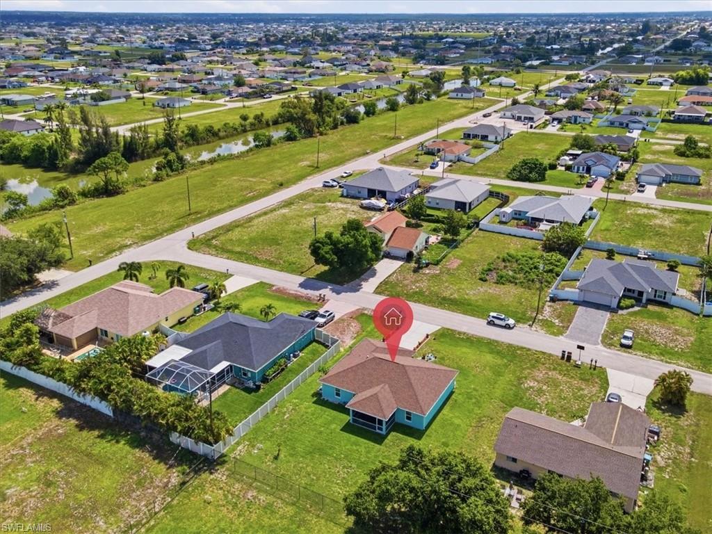 Aerial perspective showcasing a single-story residence with a light teal exterior, brown hip roof, and white-fenced perimeter