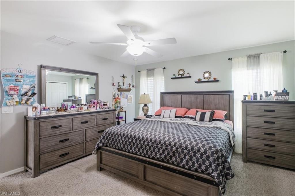 Spacious bedroom featuring light neutral wall tones, textured carpeting, and a ceiling fan