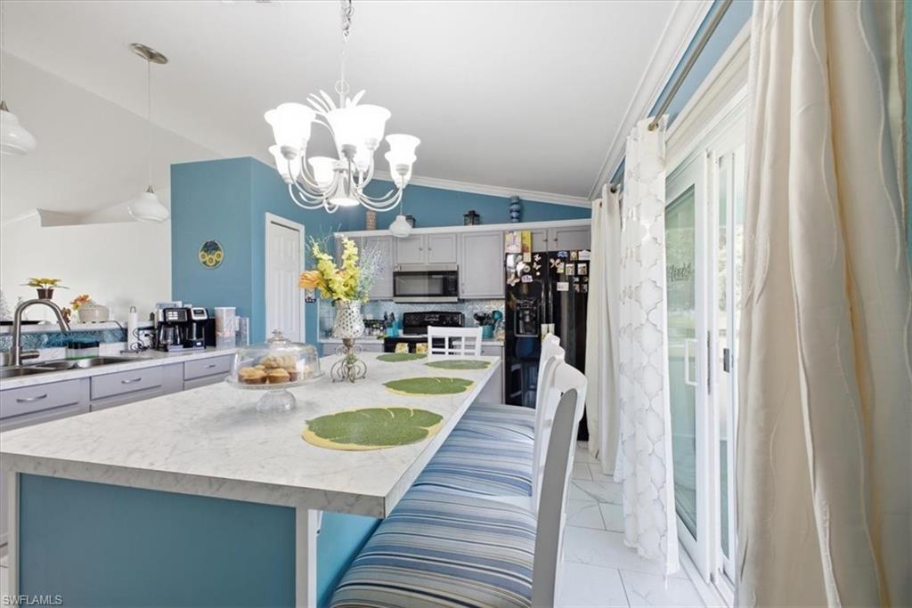 Spacious kitchen featuring a large island with a light-toned countertop, a stainless steel sink with a high-arc faucet, and white cabinetry