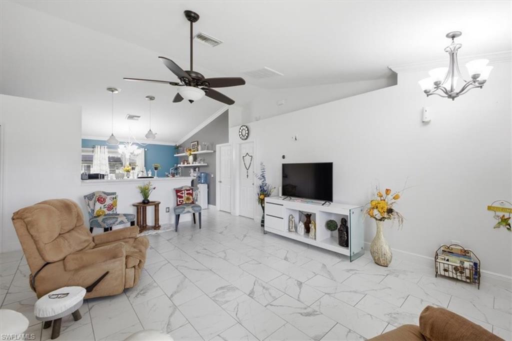 Vaulted ceilings highlight the spacious living area featuring large format tile flooring, a contemporary ceiling fan, and a chandelier