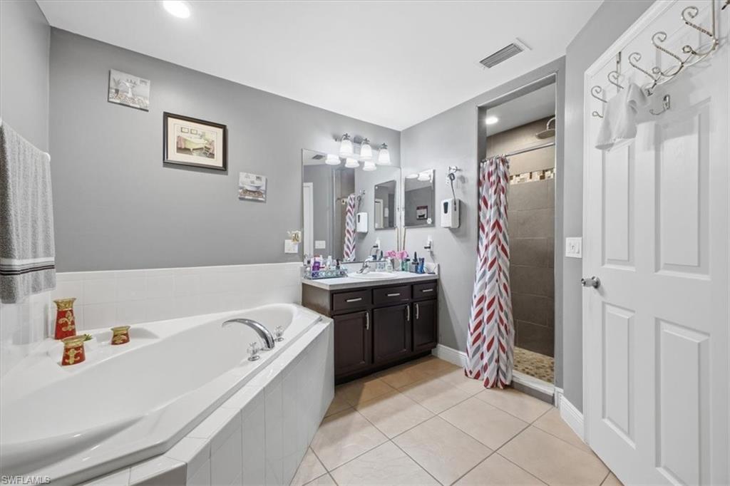 Spacious bathroom featuring a built-in corner soaking tub, dual sink vanity with dark wood-finish cabinetry, and a walk-in shower with tiled walls and a pebble-finish floor