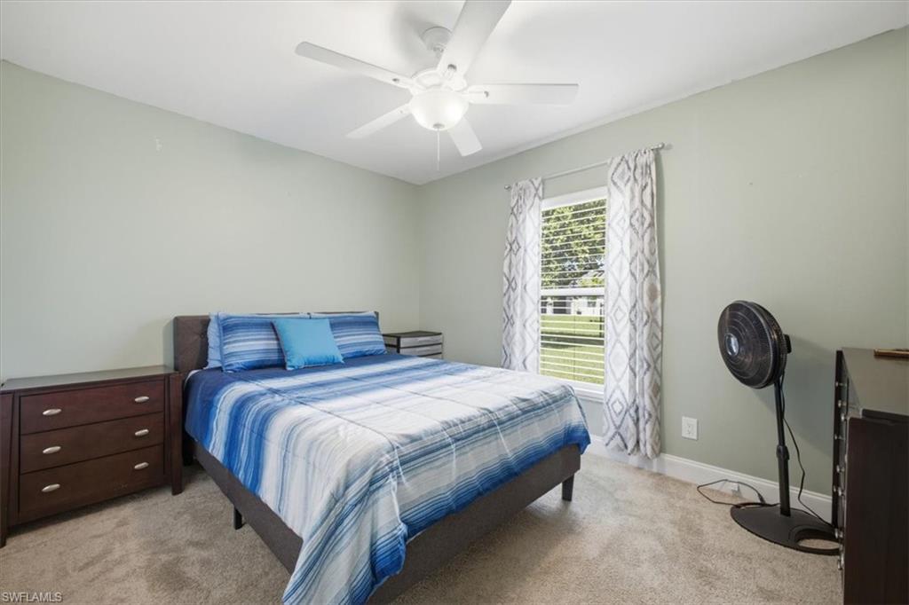 Carpeted bedroom featuring a ceiling fan, light green wall paint, a window with horizontal blinds, and baseboard trim