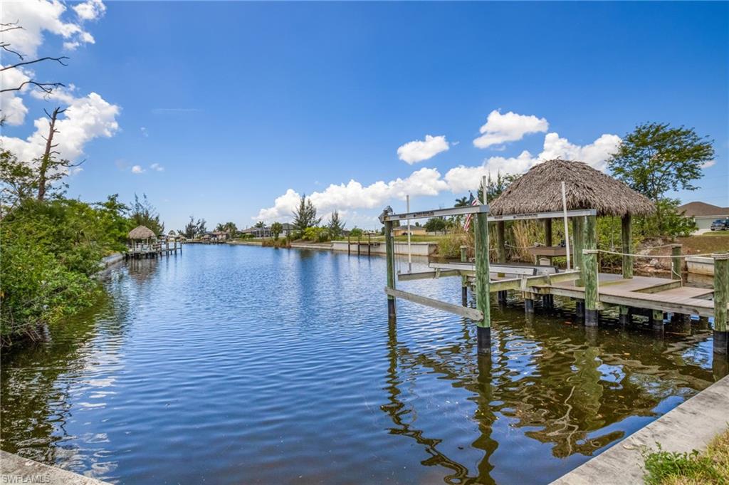 Waterfront canal with a built-in wooden dock featuring a thatched-roof tiki hut, boat lift, and concrete seawall