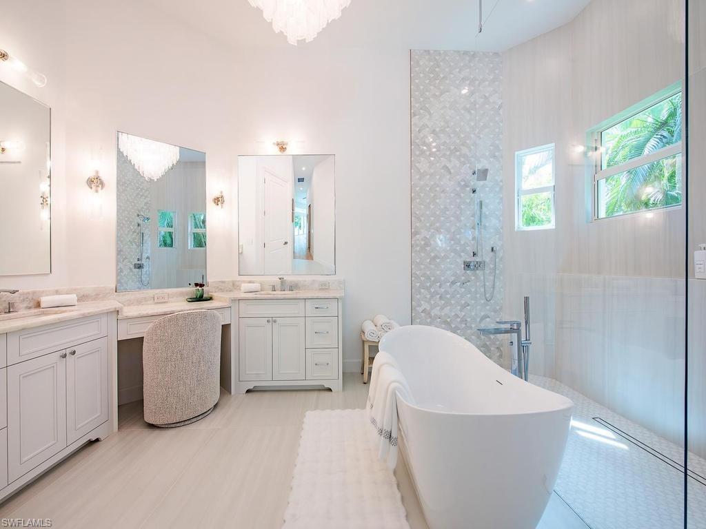 Spacious bathroom featuring a free-standing soaking tub, a walk-in shower with patterned tile, double vanities with stone countertops, and recessed lighting