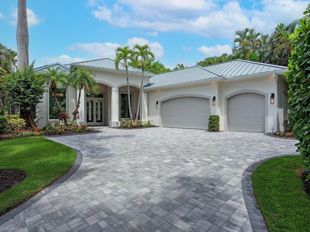 Contemporary stucco exterior featuring a metal roof, arched garage doors, and a paver driveway