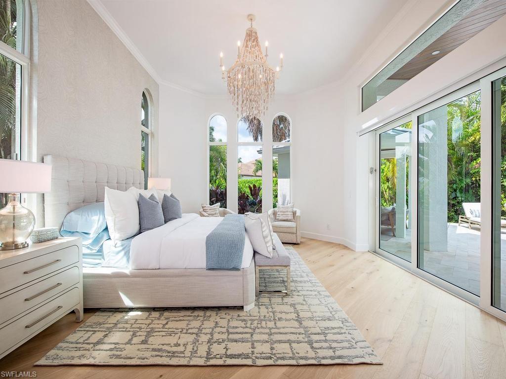 Spacious bedroom featuring light wood-finish flooring, a crystal chandelier, arched windows, and sliding glass doors opening to a paved patio