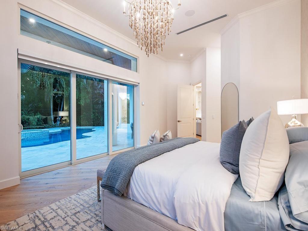 Bedroom featuring a large multi-panel sliding glass door, a transom window, wood-finish flooring, a contemporary chandelier, and recessed lighting