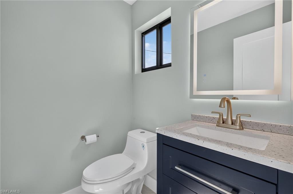 71 Mango Unit 1 Modern half-bathroom featuring a dark blue vanity with a light speckled countertop, an integrated rectangular sink, and a gold-toned faucet