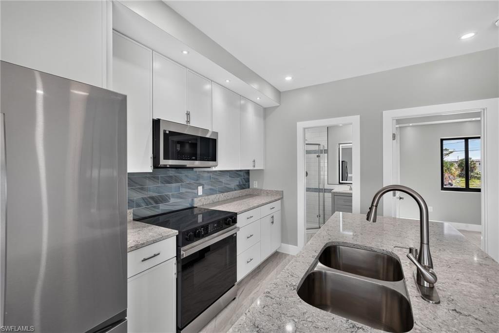 71 Mango Unit 2 Modern kitchen featuring white cabinetry, stainless steel appliances, light-toned countertops, a dual-basin stainless steel sink, and a blue tile backsplash