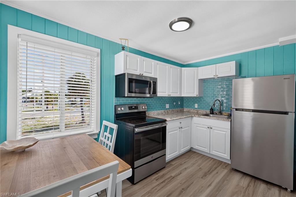 2401 Cottage Ave Unit 1 Kitchen featuring stainless steel appliances, white cabinetry, a tiled backsplash, and wood-finish flooring