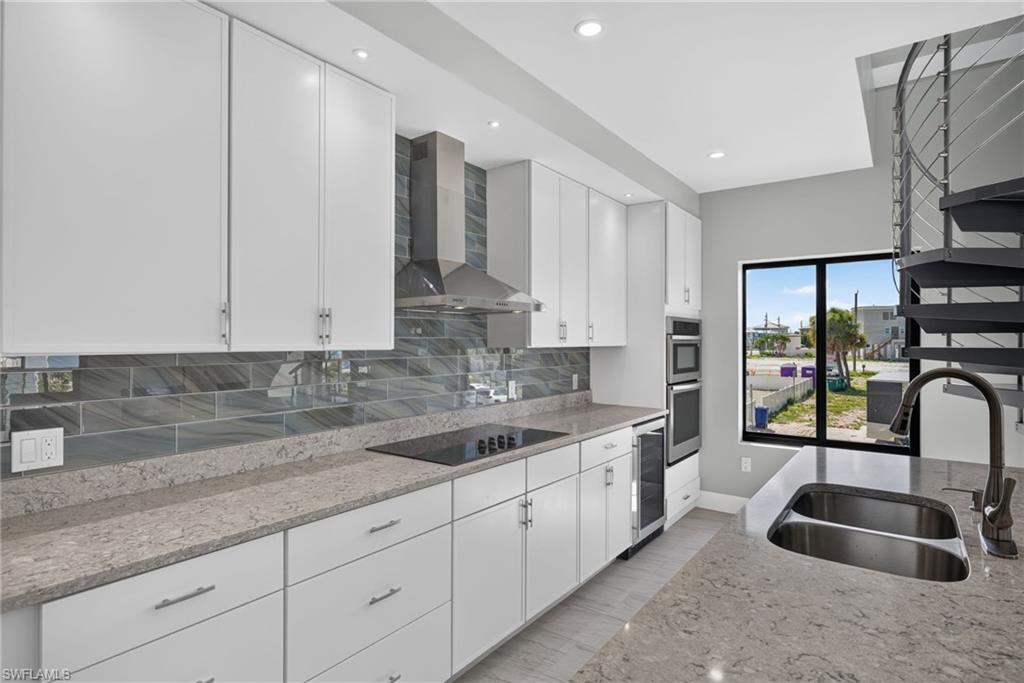71 Mango Unit 1  Modern kitchen featuring white cabinetry, integrated stainless steel appliances, a tile backsplash, and stone countertops