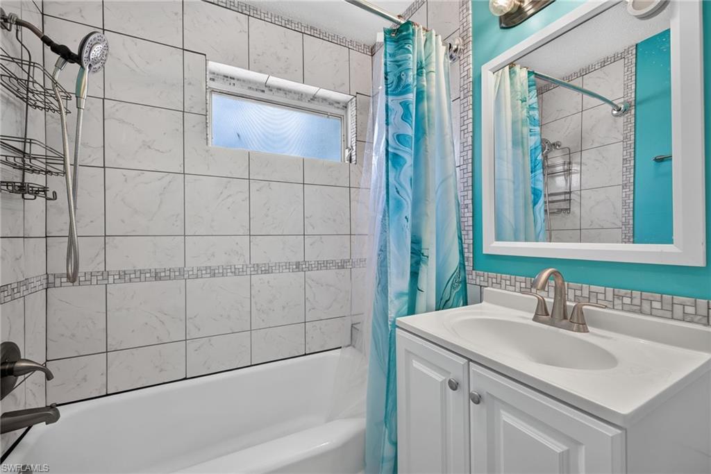 2401 Cottage Ave Unit 1 Bathroom featuring a built-in bathtub with a curved shower rod, tile surround with decorative accent, and a horizontal frosted window