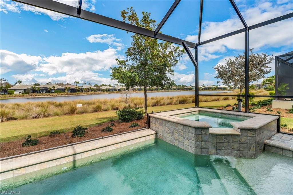 View of swimming pool with an in ground hot tub, a yard, a water view, and glass enclosure