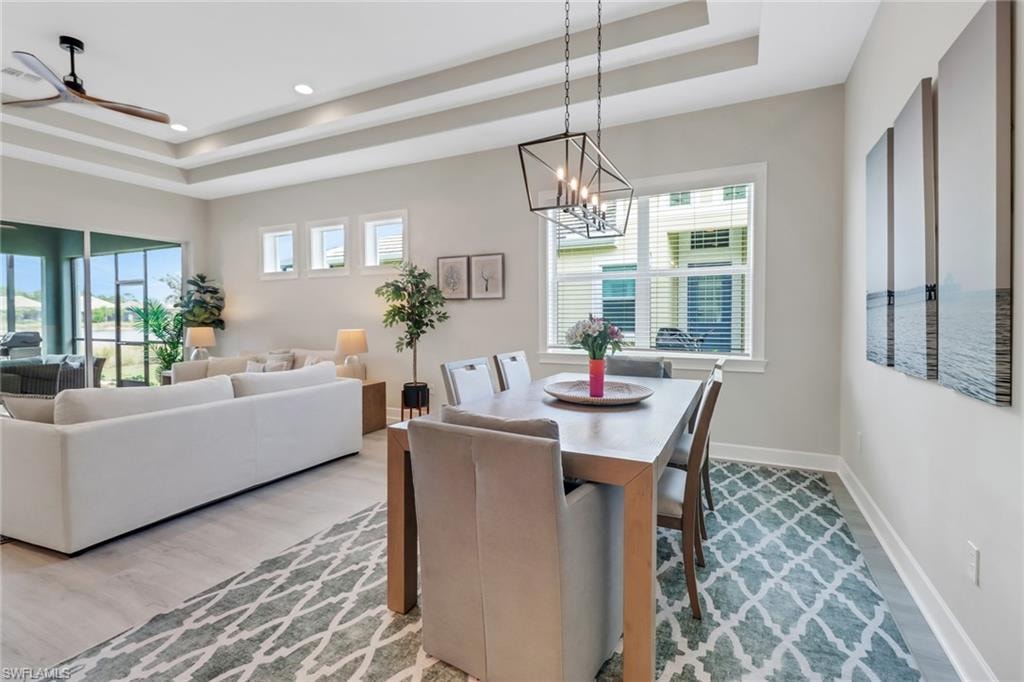 Dining space with a tray ceiling, recessed lighting, light wood-style flooring, baseboards, and ceiling fan with notable chandelier
