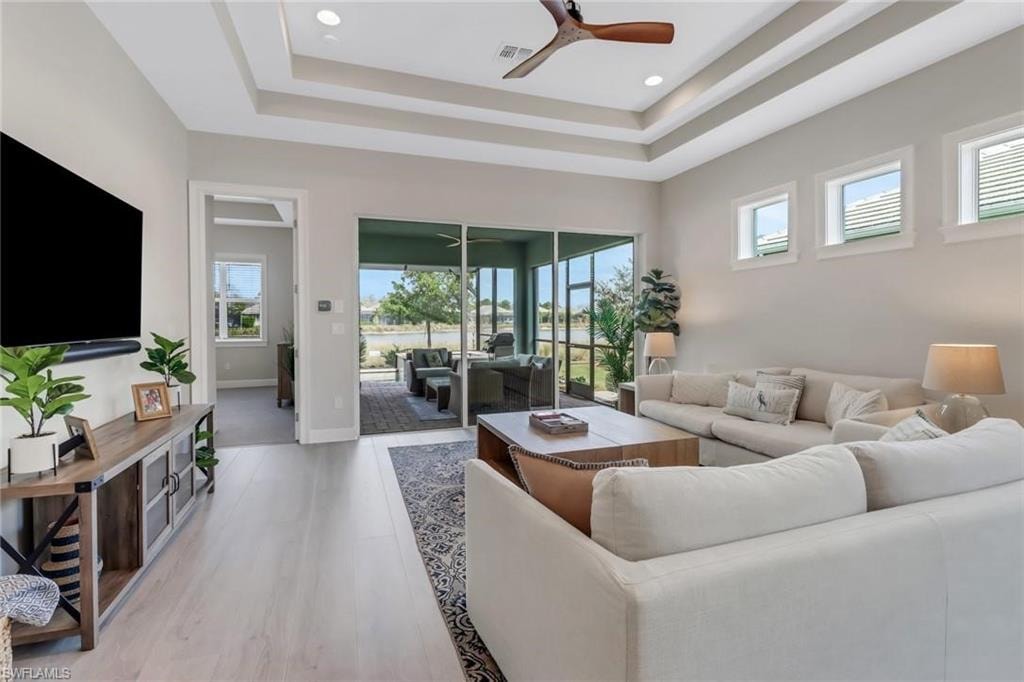Living room with a tray ceiling, ceiling fan, and light wood-style flooring