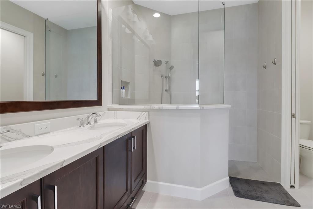 Bathroom with a walk in shower, tile patterned flooring, toilet, baseboards, and double vanity