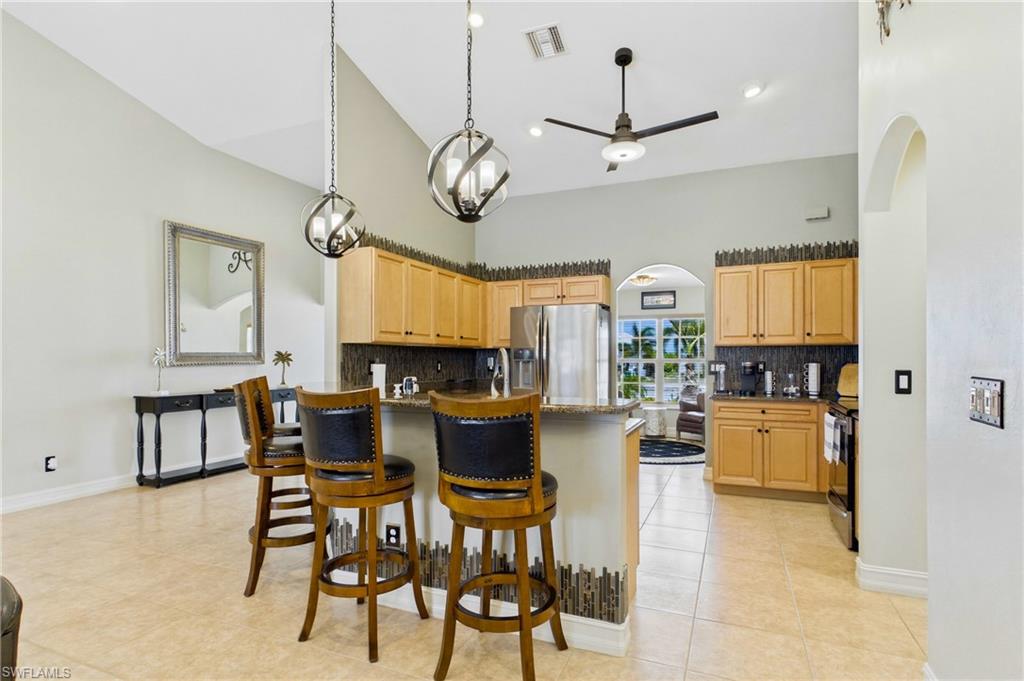 Spacious kitchen featuring light wood cabinetry, a granite-topped island with seating, stainless steel appliances, and tile flooring