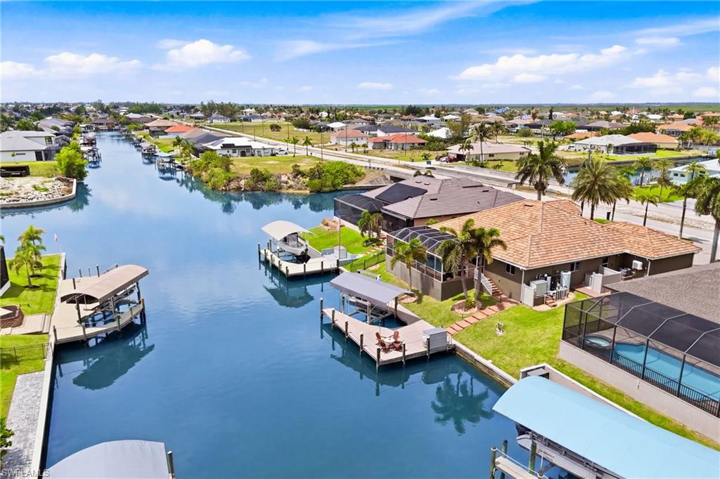 Waterfront property featuring a private boat dock with lift, screened-in swimming pool, tropical landscaping, and direct canal access