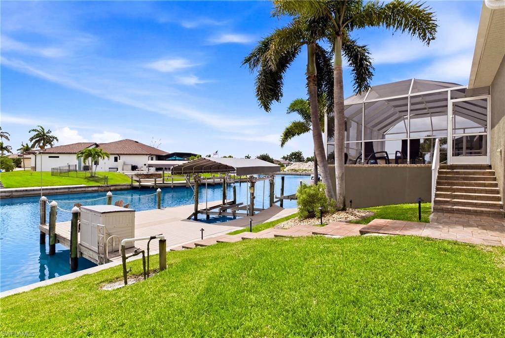 Waterfront property featuring a private boat dock with lift, screened lanai, concrete stairs, and mature palm trees