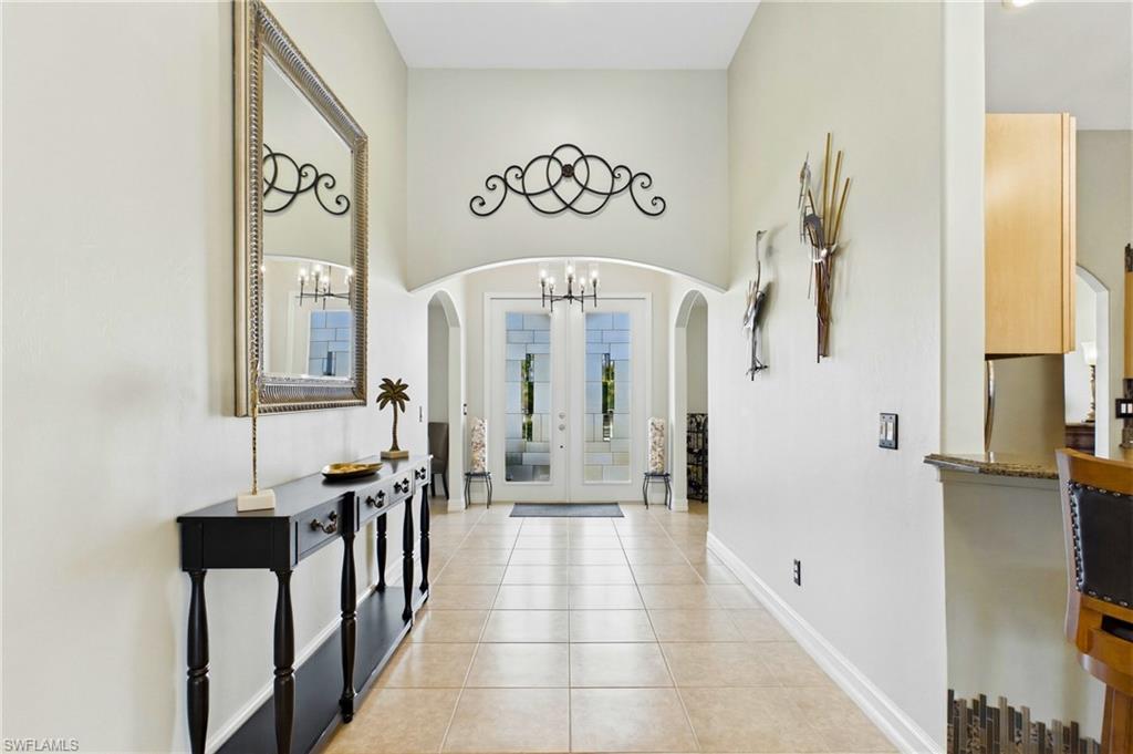 Spacious entryway featuring light-toned tile flooring, vaulted ceilings, arched doorways, and double glass-paneled entry doors